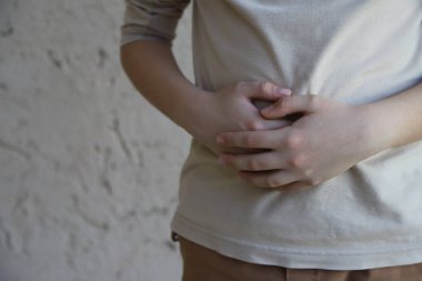 Sindirim sorunları olan hasta çocuk. Midesi ağrıyan bir çocuk. Mide sorunları olan bir genç. Gastrobağırsak hastalığı. Kopyalama alanı ve ışık renklerine sahip resim.