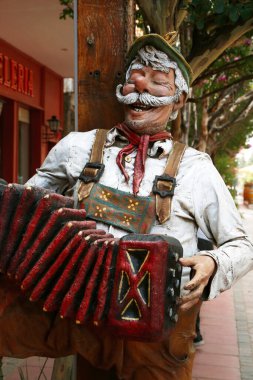 Tipik kıyafetler giyen ve akordeon çalan bir Alman 'ın oyulmuş ahşap heykeli. Villa General Belgrano 'da Heykel, Crdoba, Arjantin.