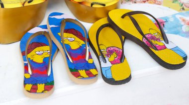 Simpsonlar 'ın karakterleriyle parmak arası terlikler. Homer ve Lisa Simpson. Plaj ve havuz için yaz ayakkabıları. Eğlenceli tasarımlar. Televizyon karakterleri. Bir mağazada satılık ürünler.