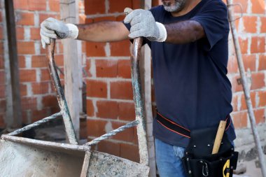 İnşaat alanında el arabasını boşaltan tuğlacı. İnşaat işçisi. İnşaatçı. Mimarlık, endüstri, iş, araçlar kavramı.