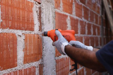 Elektrikli matkapla duvarı delen bir işçi. İnşaat alanında çalışan bir inşaatçı. Delme aracıyla insan ellerine yakın çekim. İnşaat, montaj, mimari, endüstri kavramı.