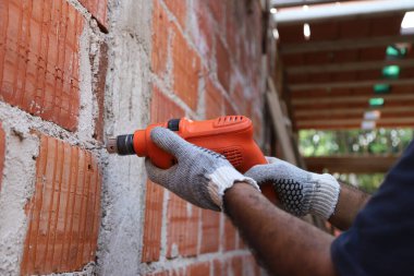 Delme aracıyla insan ellerine yakın çekim. İnşaat, montaj, mimari, endüstri kavramı. Elektrikli matkapla duvarı delen bir işçi. İnşaat alanında çalışan bir inşaatçı.