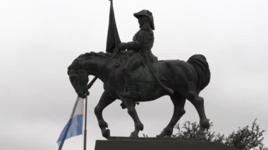 Manuel Belgrano 'nun at sırtında elinde Arjantin bayrağı ve mavi gökyüzünün üzerinde dalgalanan açık mavi ve beyaz bayrağıyla binicilik heykeli videosu..