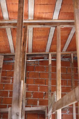 İnşaat devam ediyor. Ahşap kirişleri ve direkleri destekleyen kırmızı seramik tuğla çatı. İnşaat endüstrisi. Dikey resim.