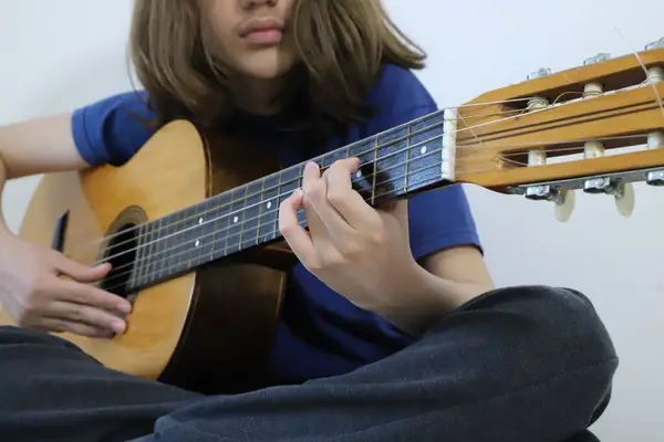 Klasik gitar çalan uzun saçlı genç bir çocuk. Müzik dersleri alan bir öğrenci. Telli alet. Kopyalama alanı olan arkaplan.