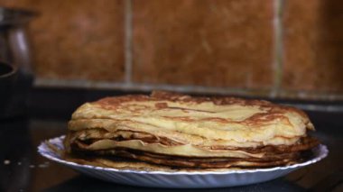 Üzerine başka bir krep konulmuş bir tabak krep yakın çekim. Maslenitsa kutlaması için hazırlık. Kahverengi fayanslı ev mutfağının arka planı.