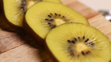 Kivi meyvesi, ince dilimlere bölünmüş. Ahşap mutfak tahtasının üzerinde duran kivi dilimlerinin yakın görüntüsü. Kamera aşağıdan yukarıya doğru hareket ediyor. Sağlıklı yaşam tarzı, ev yemeği konsepti..