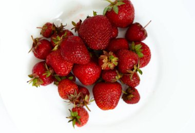Beyaz bir fincan tabağında taze olgun doğal çilek yığını. Taze toplanmış bahçe çilekleri. Soyut bir arkaplanda çileklerin detaylı fotoğrafı. Görüntüyü kapat