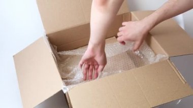 Adamın elleri, hava kabarcıklı film ve oyuncak yastığı açık karton kutuya koyuyor. Beyaz arka plan. İzole edilmiş.