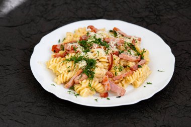 Beyaz çay tabağında makarna, peynir ve dereotlu makarna. Karanlık ve soyut bir arkaplanda. Ev yemeği konsepti. 