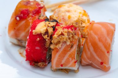 Karton tabakta servis edilen somonlu lezzetli Philadelphia suşi ruloları ve ahşap yemek çubukları. Evde suşi yiyordum. Görüntüyü kapat