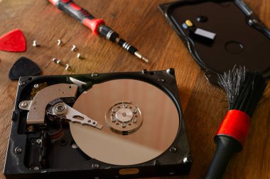 Parçalanmış bir hard disk ve bakım araçları. HDD açıldı, tornavidayla açıldı. Tahta bir masaya uzan. Sabit diskten veri kurtarılıyor. Bilgisayar donanım onarım kavramı