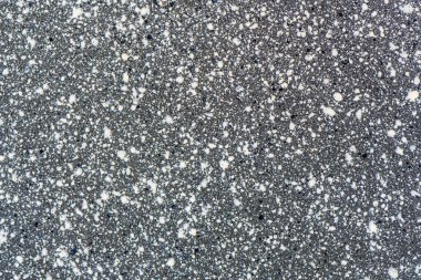 Koyu gri asfaltın yakın görüntüsü, benekli dokusu olan beton yüzey. Yüzeyde küçük beyaz ve açık gri lekeler. Soyut arkaplan. Tasarım, inşaat, kentsel çevre kavramları.