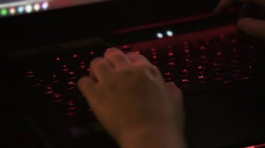 Ellerin loş, kırmızı renkli bir ortamda klavyeye yazı yazması. Geç saatlere kadar çalışma alanı. Görsel olarak çarpıcı, düşük ışık ayarında yazma eylemi. Çalışma, oyun, gece yarısı üretkenlik kavramları.. 