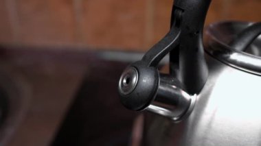 Buharla kaynayan çaydanlık. Siyah saplı metal bir çaydanlık ve kapaklı bir çıkıntı. Mutfak malzemeleri, sıcak içecekler.