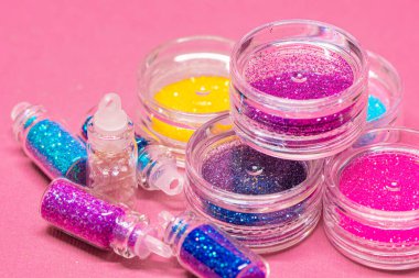 Pembe bir yüzey üzerinde çeşitli renklerde simlerle dolu küçük plastik kaplar koleksiyonu. Parıltının canlı ve çeşitli renkleri. El işleri, makyaj, dekorasyon kavramları