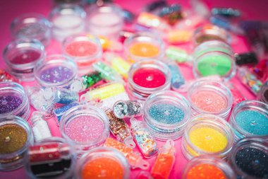 Pembe bir yüzey üzerinde çeşitli renklerde simlerle dolu küçük plastik kaplar koleksiyonu. Parıltının canlı ve çeşitli renkleri. El işleri, makyaj, dekorasyon kavramları