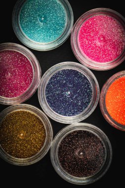 Siyah bir yüzey üzerinde çeşitli renklerde simlerle dolu küçük plastik kaplar koleksiyonu. Parıltının canlı ve çeşitli renkleri. El işleri, makyaj, dekorasyon kavramları