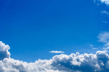 Geniş, parlak, berrak mavi bir gökyüzünün geniş bir görüntüsü. Çerçevenin altında büyük, tüylü beyaz kümülüs bulutları oluşmuş. Görüntü geniş bir his veriyor, üst kısımda geniş bir kopya alanı var..