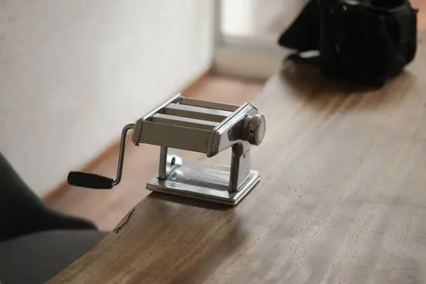 Tahta bir masanın üzerindeki metal makarna makinesinin dikey görüntüsü.