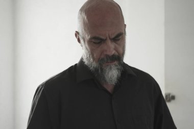 Sakallı, kel, uzun saçlı olgun bir adam.