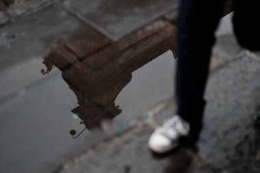 Siyah elbiseli, şemsiyeli ve bina yansımalı bir adamın silueti.