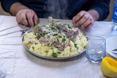 hot fresh mansaf steam with hands around it ready to be eaten on family table for iftar clipart