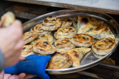 Yaşlı adam elinde alüminyum tabak dolusu beyaz peynirli hamur işi tutup eski fırına koyuyor.