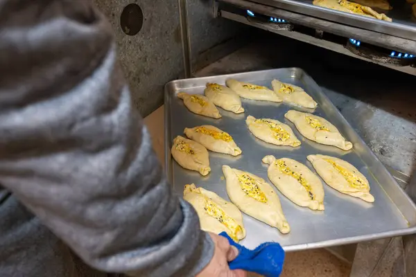 stock image Old man hands holding aluminum plate full of white cheese stuffed pastries and putting it in old oven