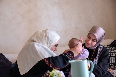Anne ve büyükanne güzel giysiler içinde bebekle oynuyorlar. Çocuklarla geçirdikleri anların tadını çıkarıyorlar.