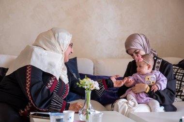 Anne ve büyükanne güzel giysiler içinde bebekle oynuyorlar. Çocuklarla geçirdikleri anların tadını çıkarıyorlar.
