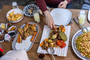 Müslüman bir aile dikdörtgen bir masa etrafında toplanıyor, birlikte doyurucu bir yemek yiyorlar, çeşitli yaşlardaki üyeler bu olayın sıcaklığını ve neşesini artırıyorlar.