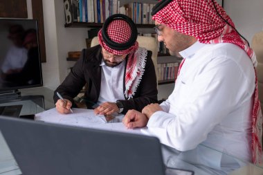 Arap erkekler dizüstü bilgisayar ve kağıtlarla proje üzerinde çalışırken, sonuçları iyileştirmek için tüm olasılıkları değerlendiriyorlar.