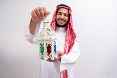 Draped in the dignified attire of Kandoura and Keffiyeh, an Arabic man extends a symbol of hospitality and generosity by holding Fanous. Against a backdrop of purity, to illuminate the essence of Eid clipart