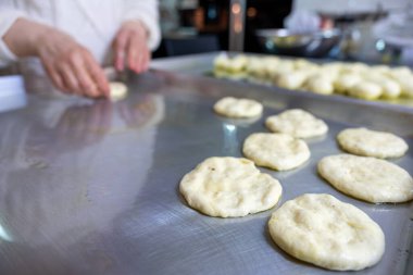 Woman kneads dough with hands in the kitchen on metal tray, pushing it to be flat while using olive oil clipart