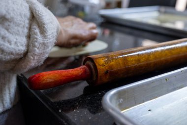 old woman hands using rolling pin to flatten the dough  on black marble  covered with oil clipart