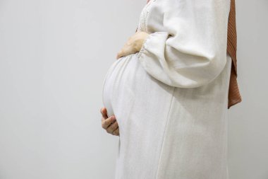 Ayrı beyaz arka planda hamile bir Arap kadın hamileliğin 9. ayında karnına dokunarak vücudunun şeklini gösteriyor.