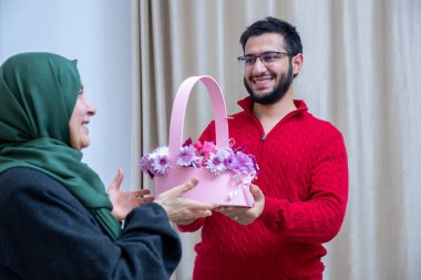 As a surprise in their home, a happy Muslim male gives roses to his mother clipart