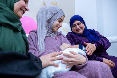 Females are celebrating new baby and holding it indoors, holding gifts and balloons are around clipart