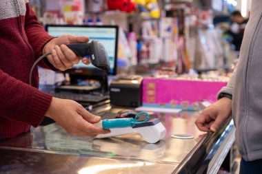 Mağaza adamı, hediye dükkanından seçilen ve arka planda POS makinesi olan ögenin barkodunu tara