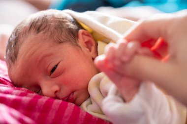 Anne yeni doğmuş bebeğini kucaklıyor. Yüzlerinde gülümseme ve bebek yüzünde sevimli bir ifade var.