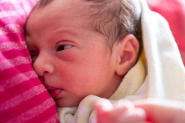 Anne yeni doğmuş bebeğini kucaklıyor. Yüzlerinde gülümseme ve bebek yüzünde sevimli bir ifade var.