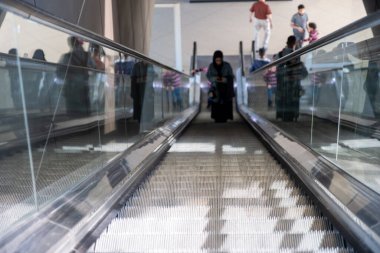 Bir üst kata çıkmak için yürüyen merdiven kullanan bir kadın.