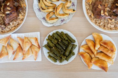 Üzüm kabı ahşap masanın üzerinde sambousek ve qatayef ile üstten görünüyor.