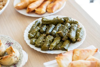 Üzüm kabı ahşap masanın üzerinde sambousek ve qatayef ile üstten görünüyor.