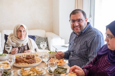 Arabian family having dinner together on wooden table with father,mother,grandfather,grandmother and son clipart