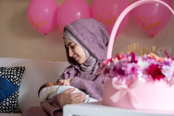 Müslüman bir kadın, doğum gününü yeni doğum günüyle kutluyor. Oturma odasında, buket ve pembe renkli balonlarla.