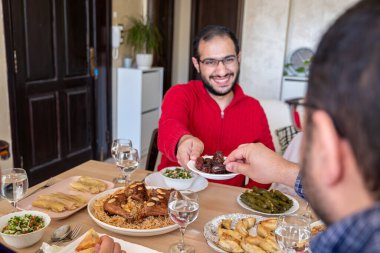 Genç bir erkek iftar sırasında ailesiyle yemek masasında buluşup, tarih veriyor.