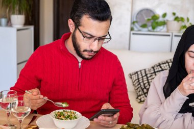 Young bearded man using smartphone while eating clipart