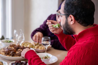 Genç sakallı adam öğle yemeği sırasında annesiyle konuşuyor.